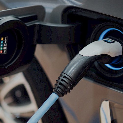 Nahaufnahme eines Elektroautos beim Ladevorgang: Ein Ladekabel ist in die Ladebuchse eingesteckt, die von einem blauen Leuchtring umgeben ist.